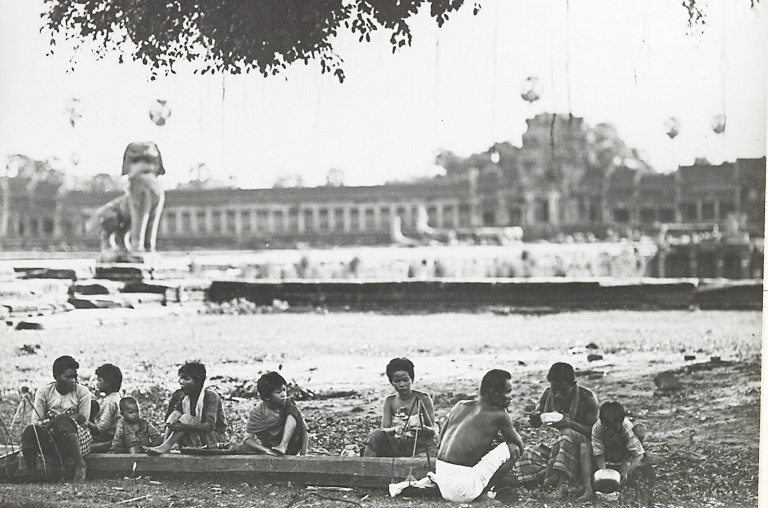 Old photograph of Cambodians sitting outside a big temple eating food